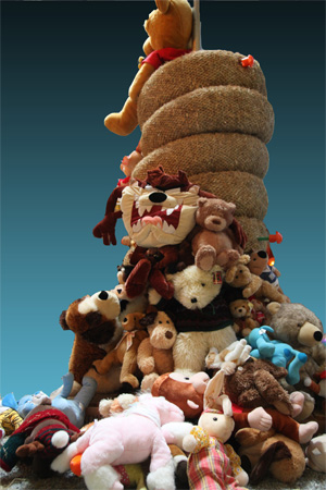 A towering pile of assorted stuffed animals, including a prominent Taz character, against a blue gradient background with a rope structure in the center