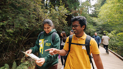 Two students smiling and pointing at a map in Muir Woods