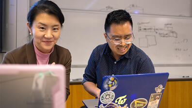 Student and professor looking at laptops and smiling