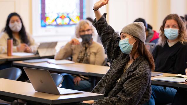 Student sitting at a table raises hand in class