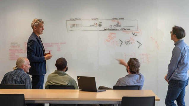 Five people collaborating in front of a white board.