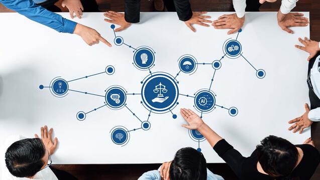 data scientists overlooking a table with various interconnected AI ethics icons with a icon featuring the scales of justice with a hand underneath