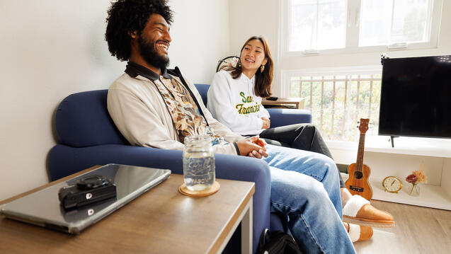 two students sit on sofa and laugh together