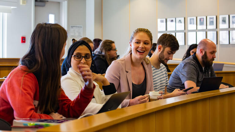 A number of students talk while seated in a jury box.