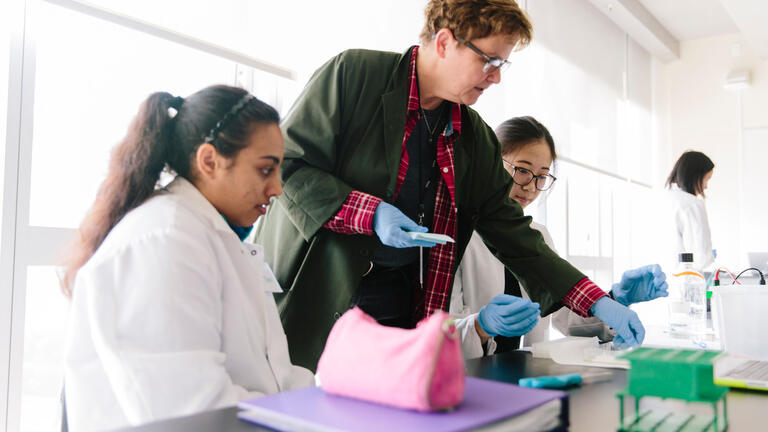 Professor assists students working at a table in a Biology lab.