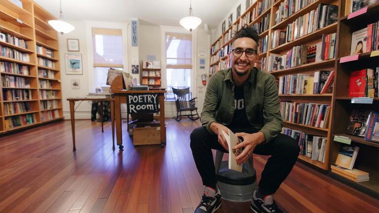 Man seated in a reading room, surrounded by books.