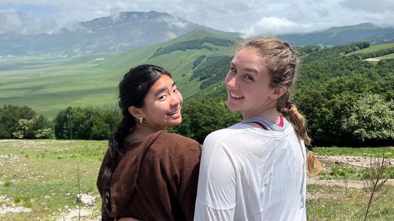 Two students sit on a hill looking over a valley