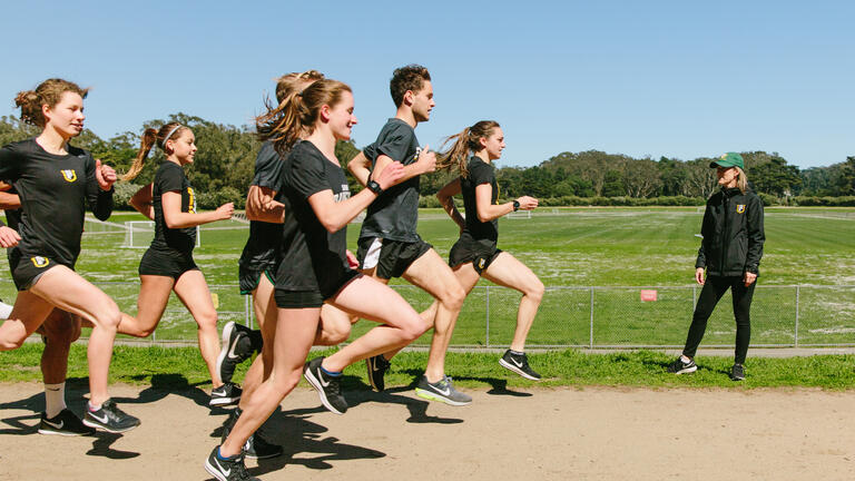 USF cross-country team running and passing by coach