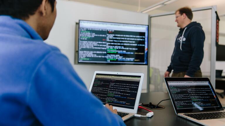 Student and professor looking at code on a computer screen.