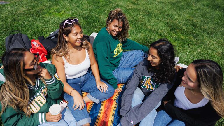 Five USF students sitting in the grass, chatting