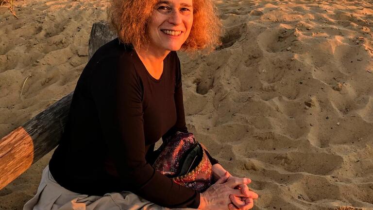 Joy Ladin sitting on a bench in the sand on the beach