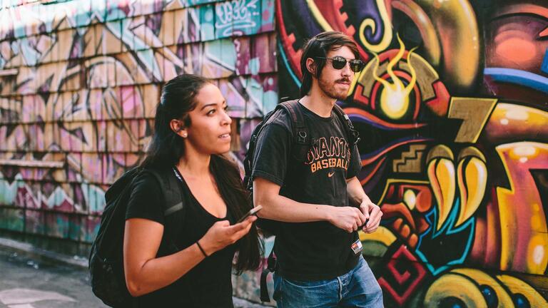 two student walk in front of a mural in SF's mission district