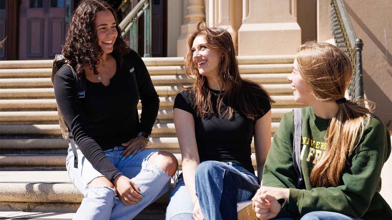 Three students sitting on steps of Lone Mountain