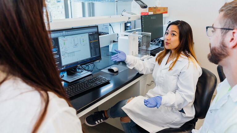 student in bio lab show data results on computer to faculty