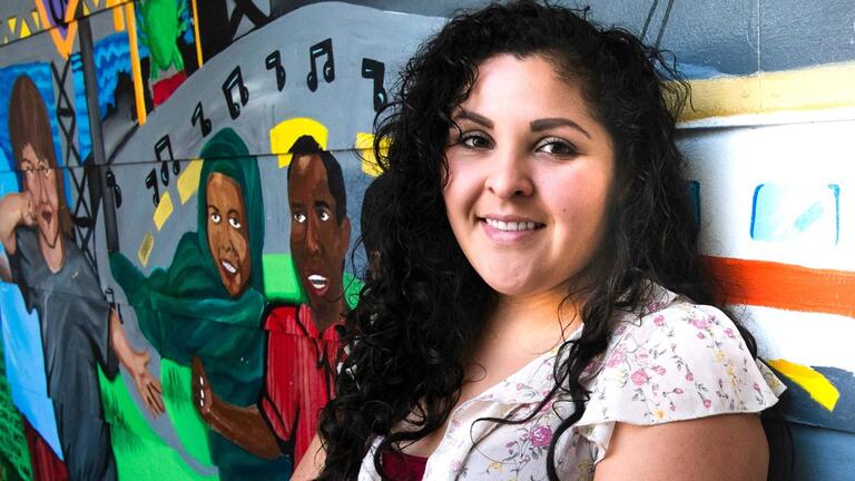 Student stands in front of a colorful mural.