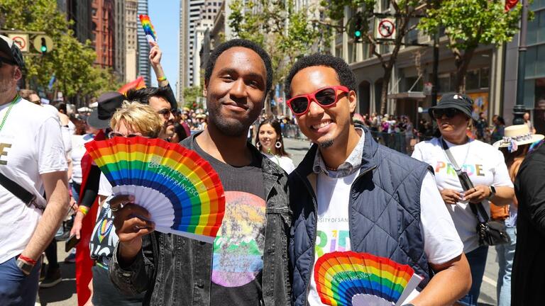 Two people holding rainbow paper fans and smiling at the Pride parade