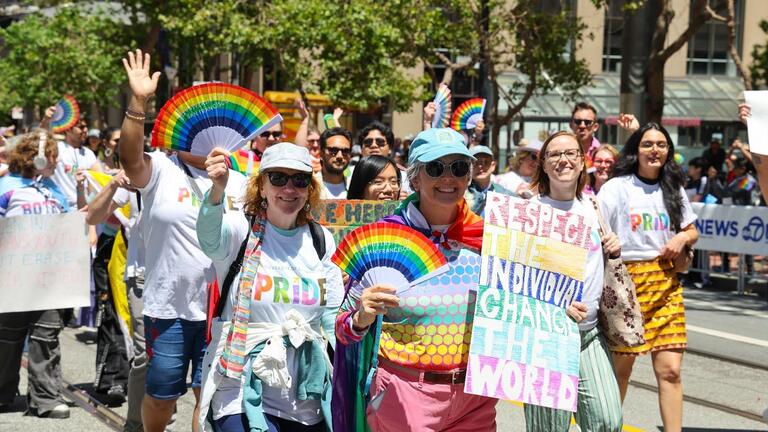 People marching and waving in the Pride parade, one person holds a sign that says "respect the individual change the world"