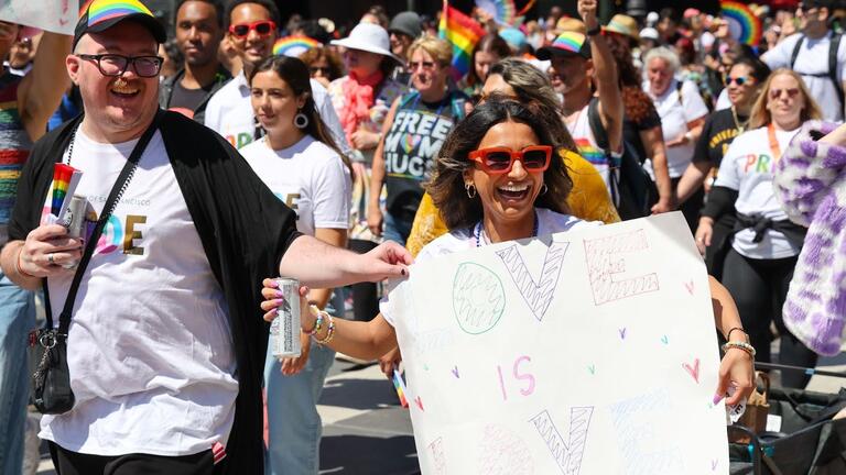 People marching in the Pride parade, one person is smiling and holding a sign that says "love is love"