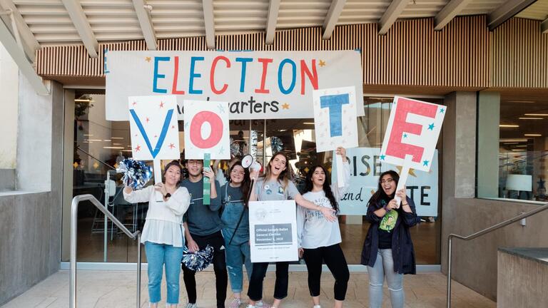 students stand in front of an Election banner holding letters VOTE 