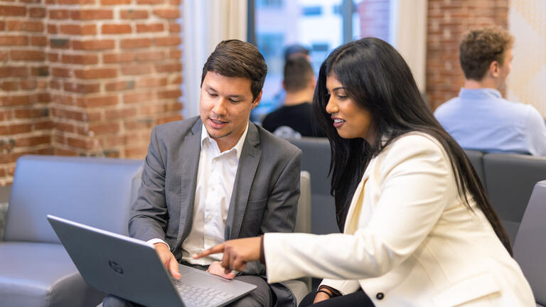 Two USF students in business attire chatting and pointing to a laptop screen