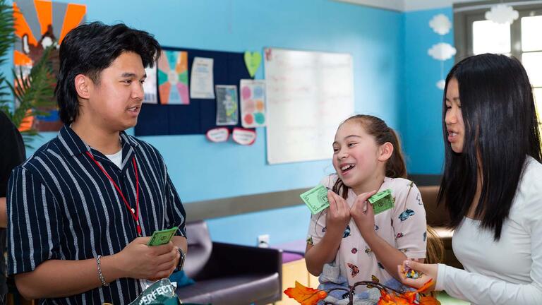 Student teaching two kids and holding fake money