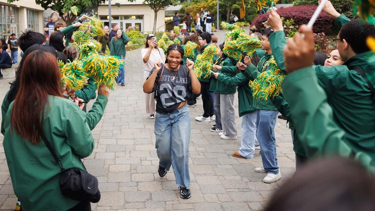 New student greeted by students waving green and yellow pom-poms