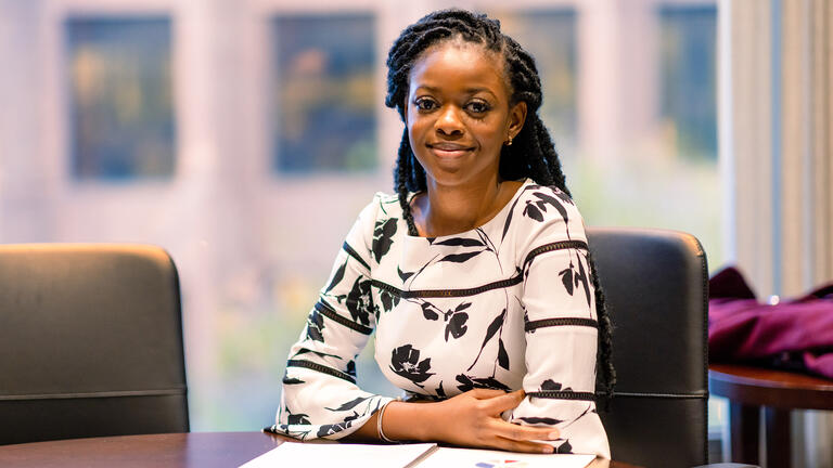 Graduate student in black in white floral shirt smiling at conference table