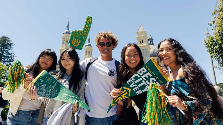 Students smiling and holding up USF spirit gear 