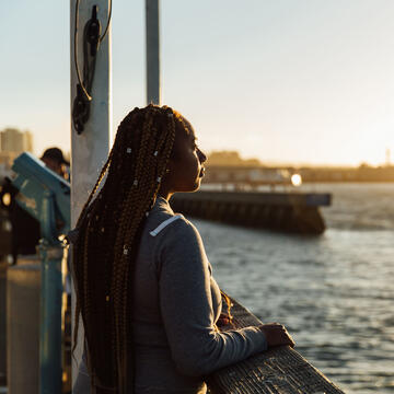 Student leans on a railing and looks over the bay at sunset.