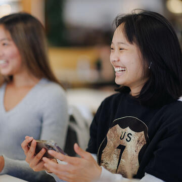 Student smiles in class while holding a phone.