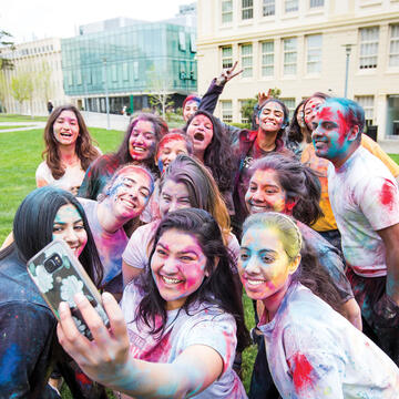 Students covered in colored power pose for a photo on the lawn.