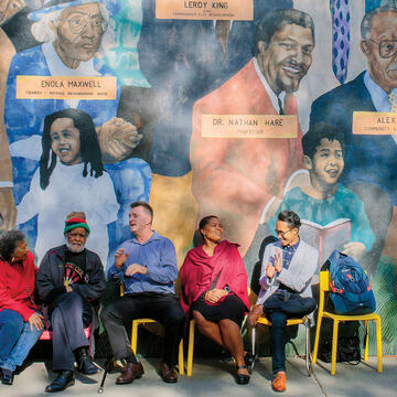 Professors, community members, and a student in front of a Western Addition mural