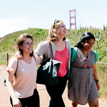 Three friends walk in a park near the Golden Gate Bridge.