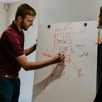 Man sketching on white board with colleague