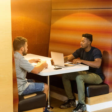 Two coworkers working on laptops sitting at a booth