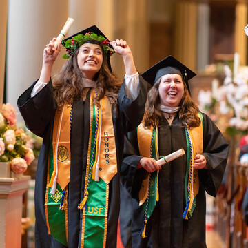 Two graduates walk down the aisle holding diplomas
