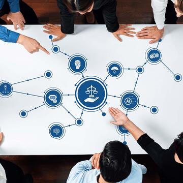 data scientists overlooking a table with various interconnected AI ethics icons with a icon featuring the scales of justice with a hand underneath