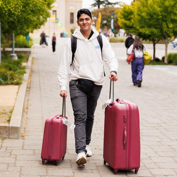 Student with two pink suitcases walking on campus path