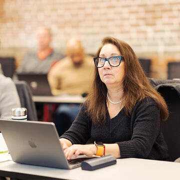 Graduate student sitting at desk in class, typing on laptop