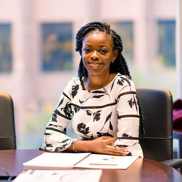 Graduate student in black in white floral shirt smiling at conference table