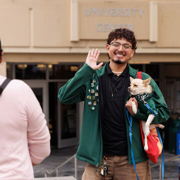 Student waves hand in the air while holding a small dog