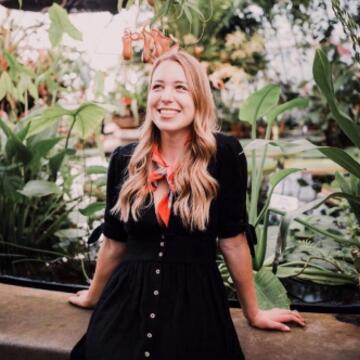 Anastasia Ecin leaning against a wall in a green house