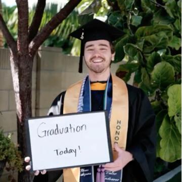 Shane Yoshiyama in graduation attire holding a sign that says Graduation Today!