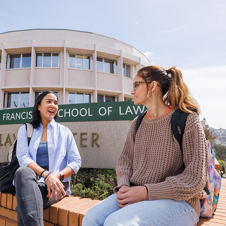 students sit in front of school of law sign on usf campus