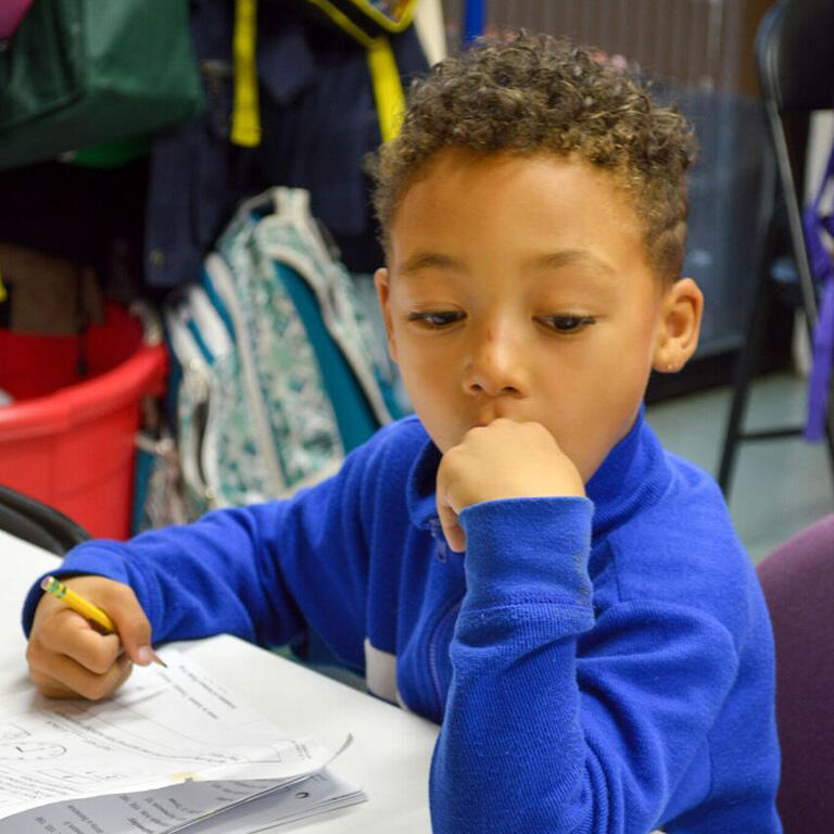 young child holds pencil in class