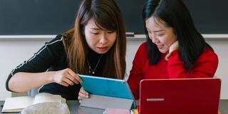 Two students look at a laptop in class.