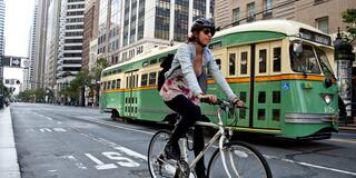 Person biking in Downtown San Francisco with a trolley behind them.