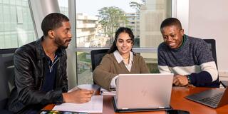 Three people are sitting at a table in a bright office