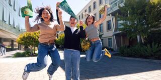 Three people jumping up in the air on campus with excitement holding USF gear