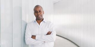 Dr. Darrick Smith leaning against a wall with arms crossed in front of him 